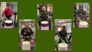 Five students play white plastic bucket drums with drumsticks. From left to right: boy, boy, girl, girl, boy.