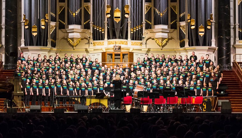 Large choral group performing on stage at Sydney Town Hall