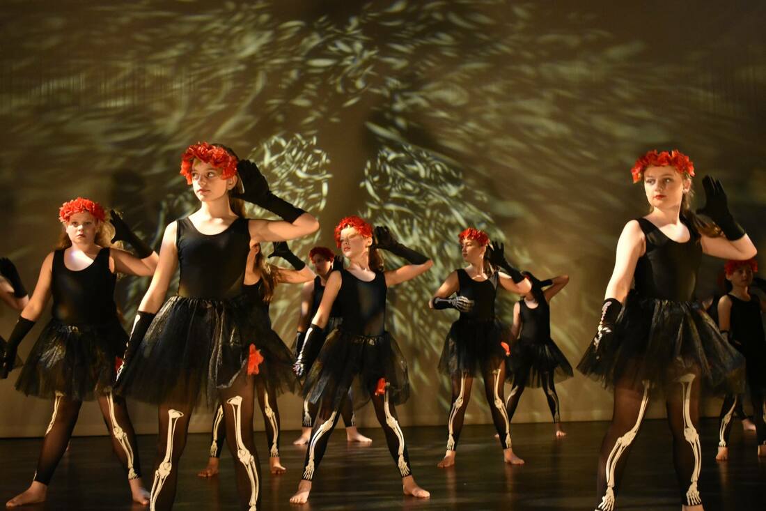 group of dancers on stage in black costumes with red headpiece