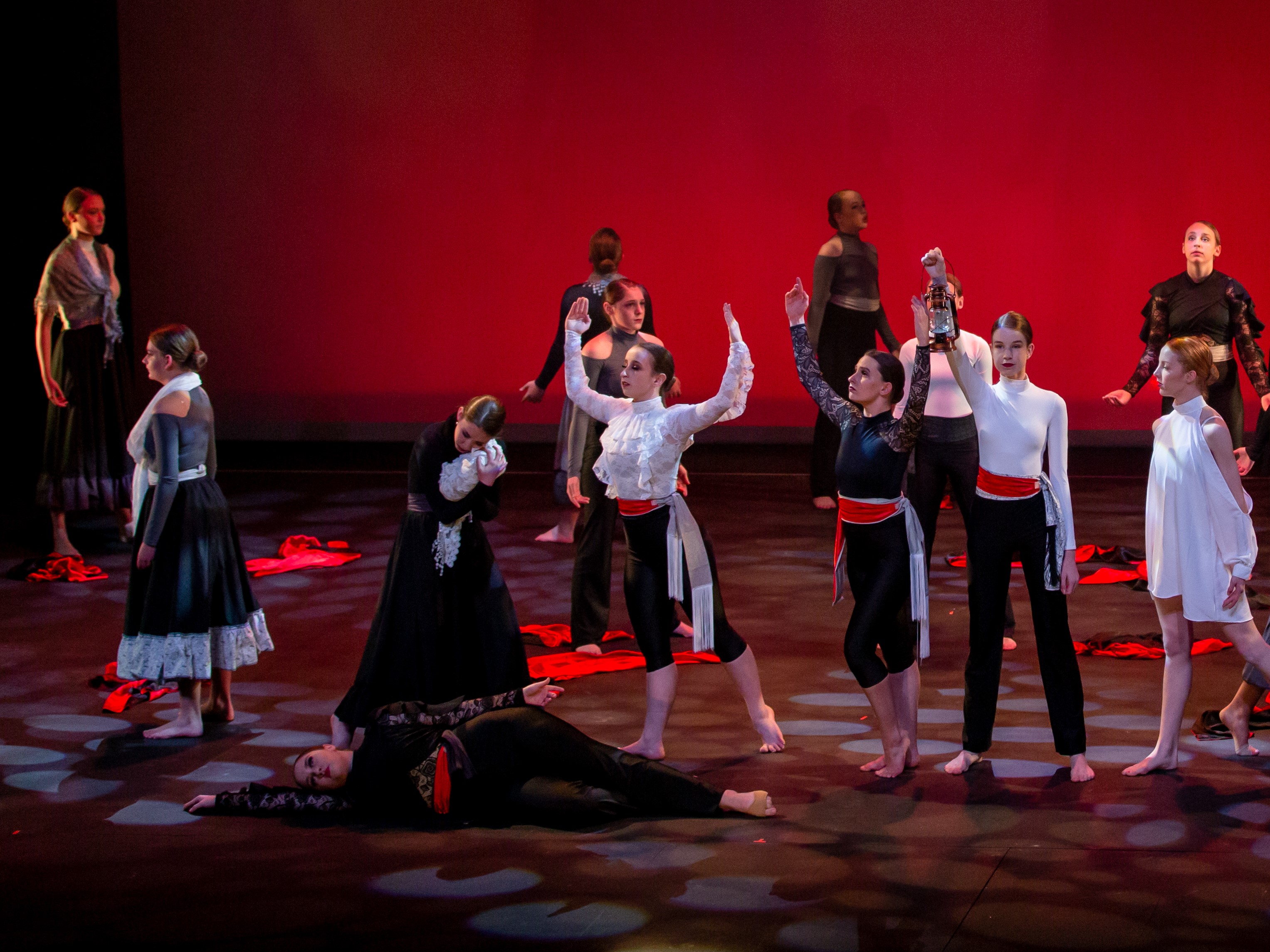 dance ensemble on stage in costumes under red lighting