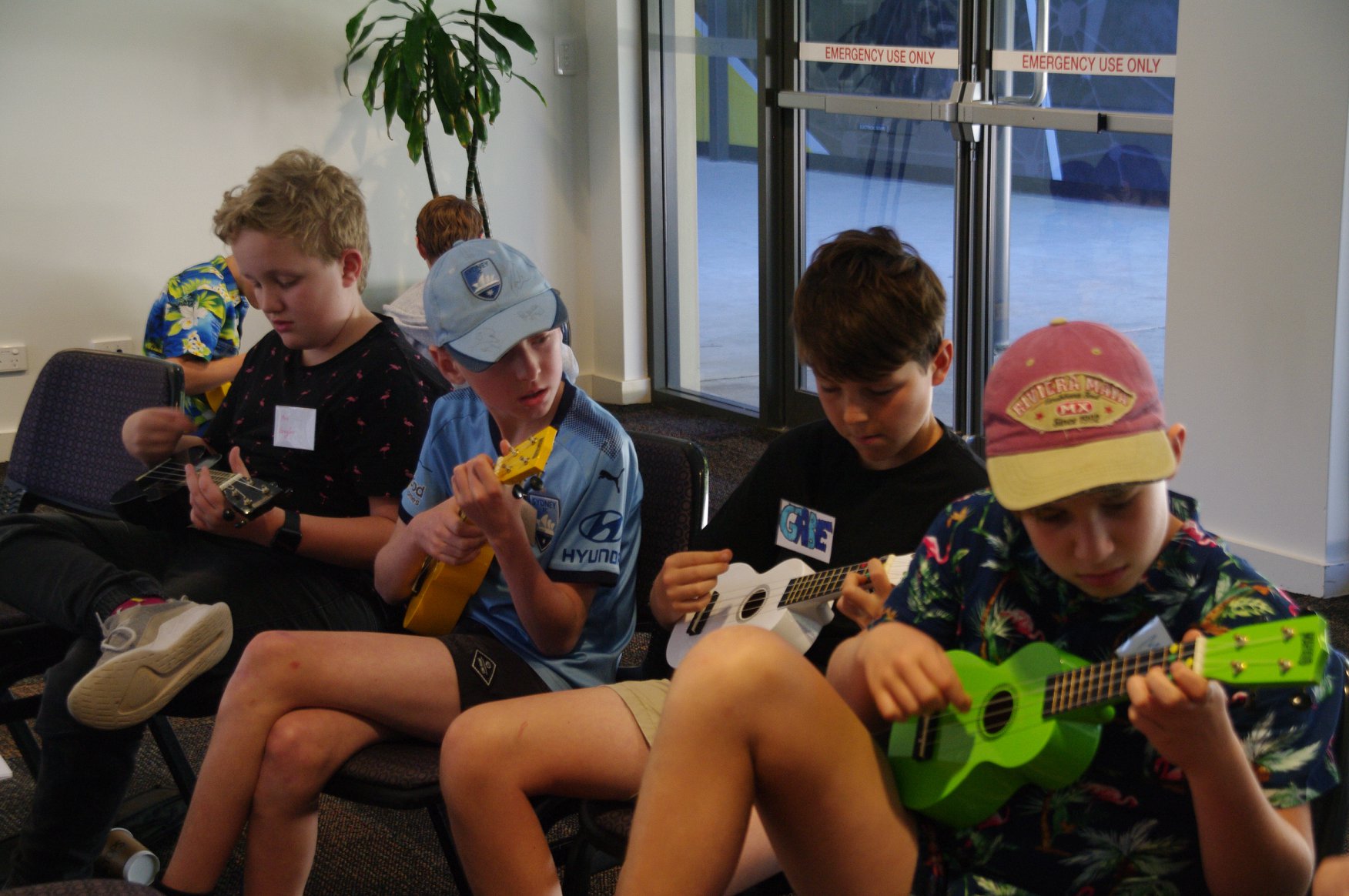 4 boys sitting on a lounge playing ukulele