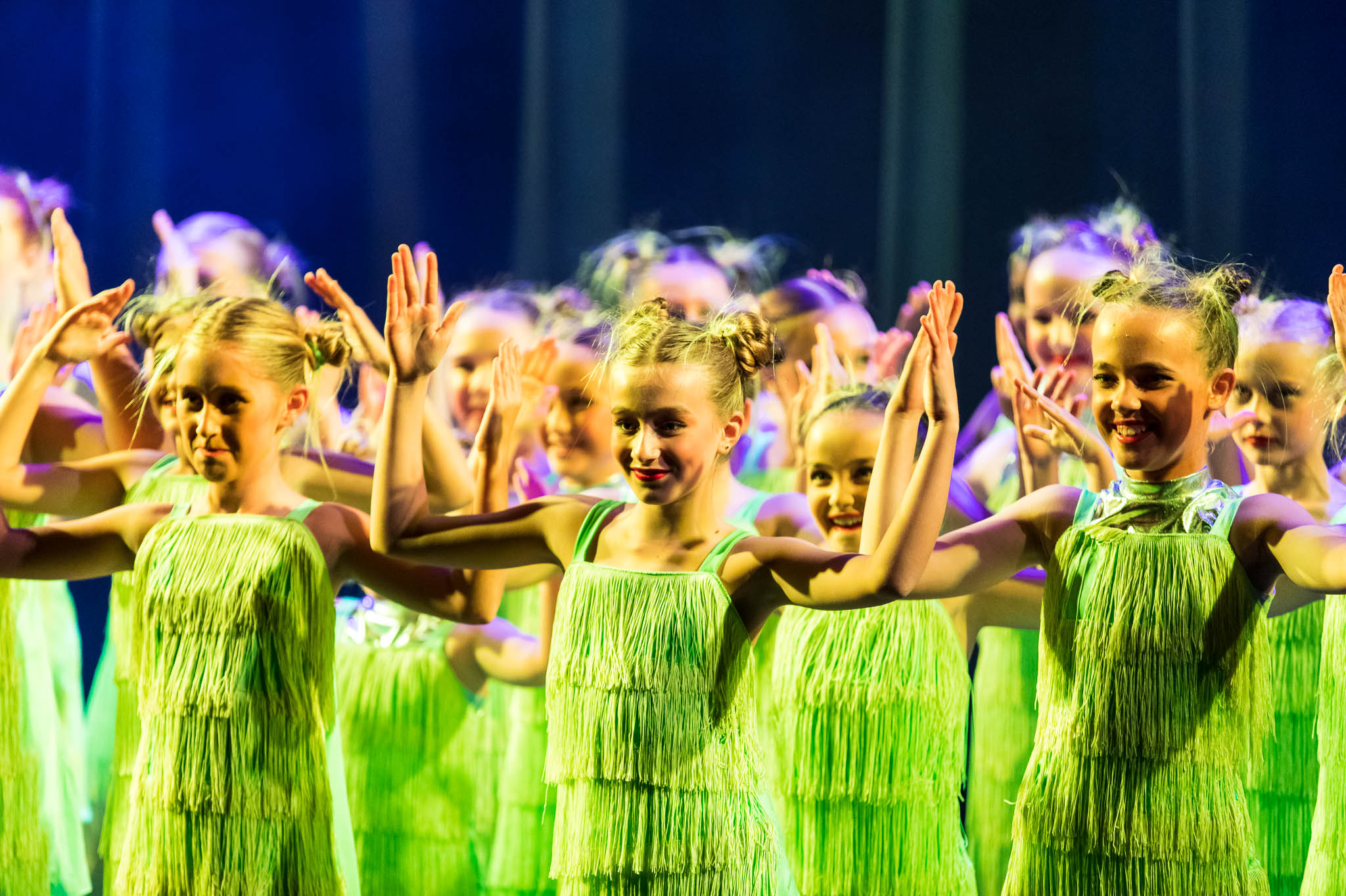 group of students in lime green fringe dresses with hands in air