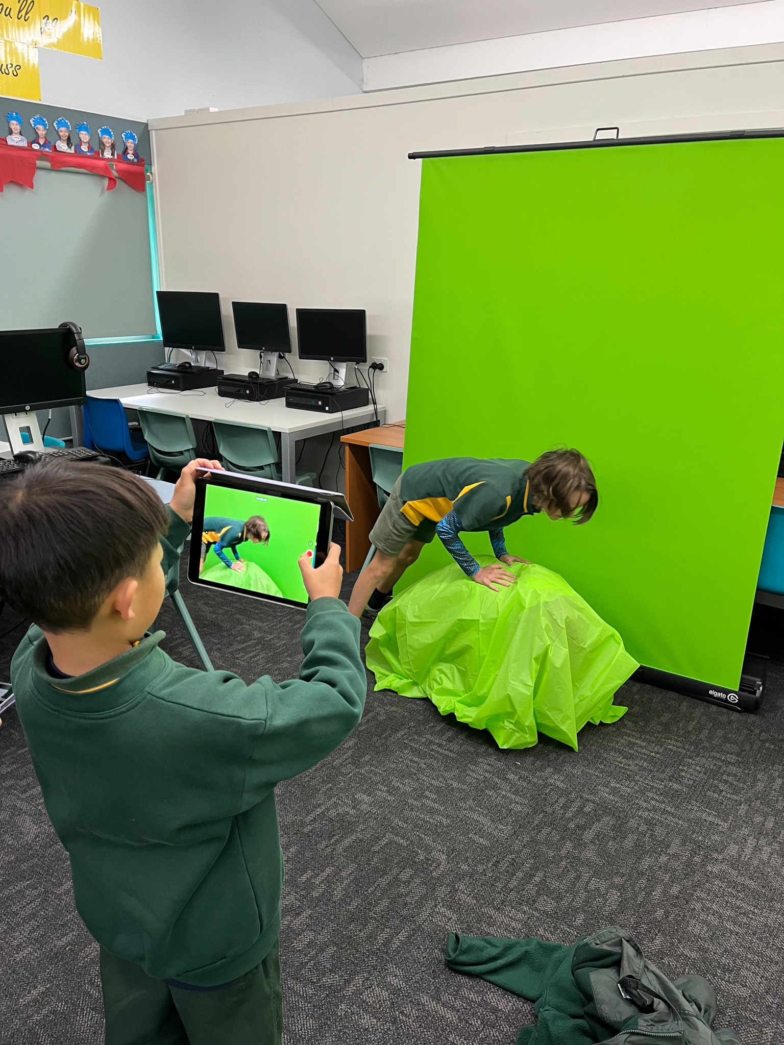 A boy using an iPad to film a scene in front of a green screen.