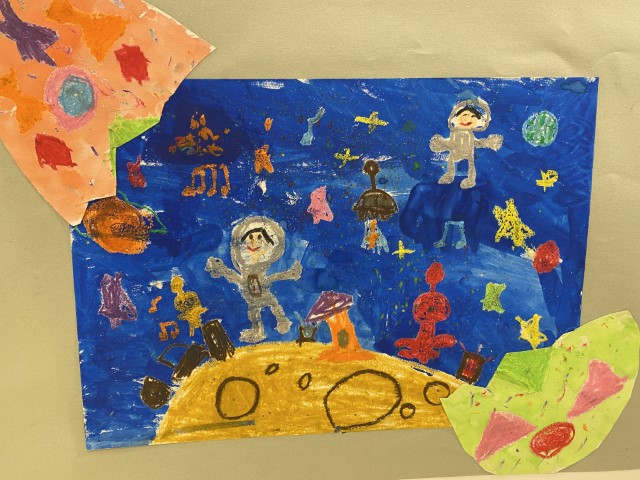 Student artwork of astronauts and aliens dancing on the yellow moon, with glistening stars, colourful music notes and bright planets in the background.