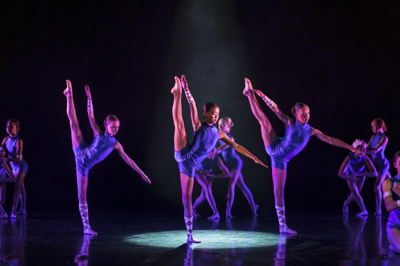 Dancers on stage in blue demitard under spotlight standing on one leg