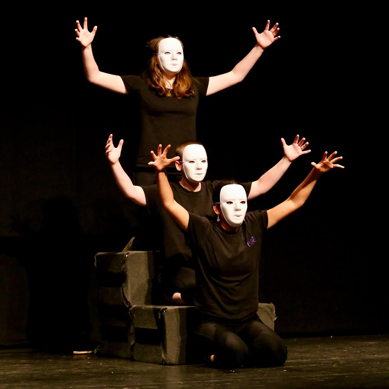 3 students one behind the other with arms outstretched wearing white masks 