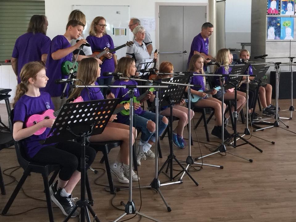 Group of students sitting on chairs playing instruments in purple tshirts