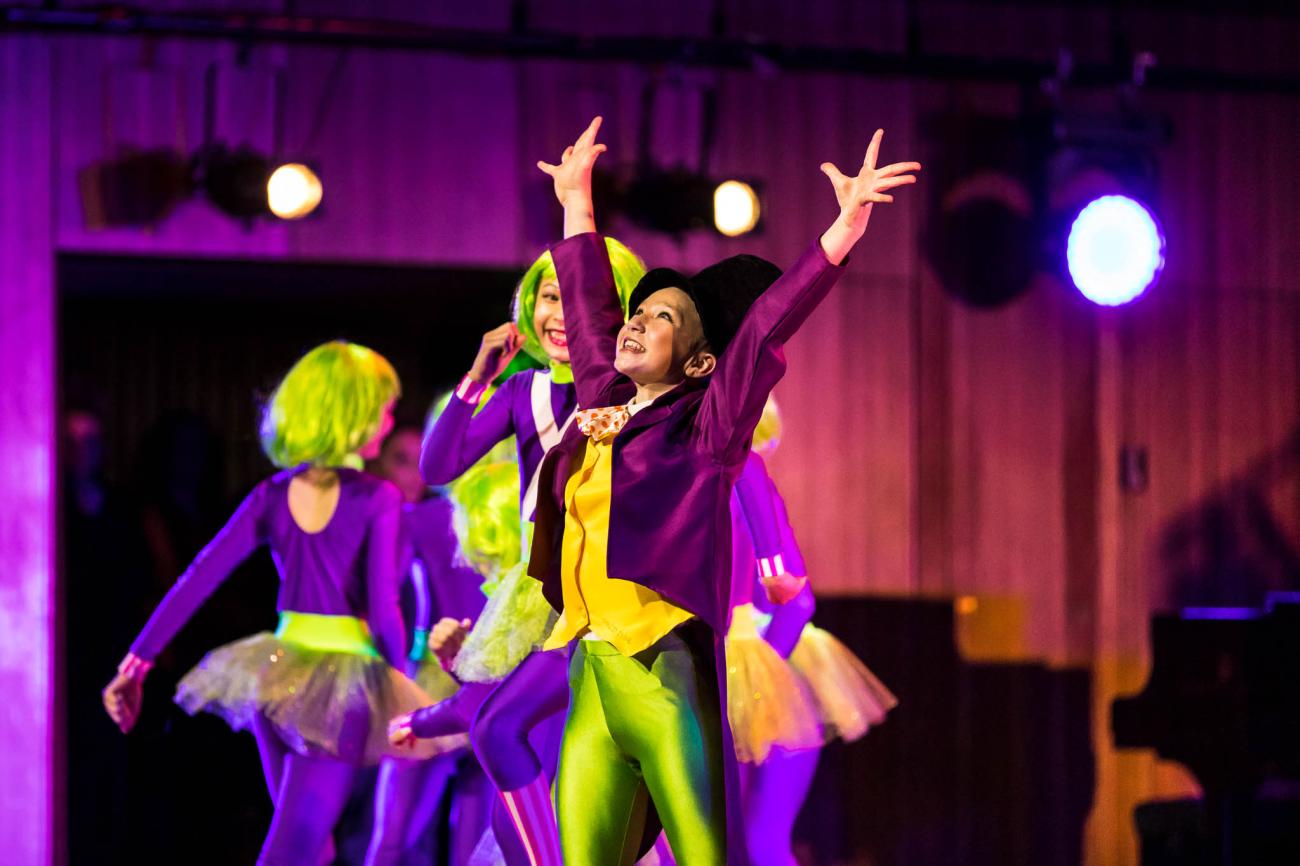 dancer on stage with arms in air with other young dancers on background