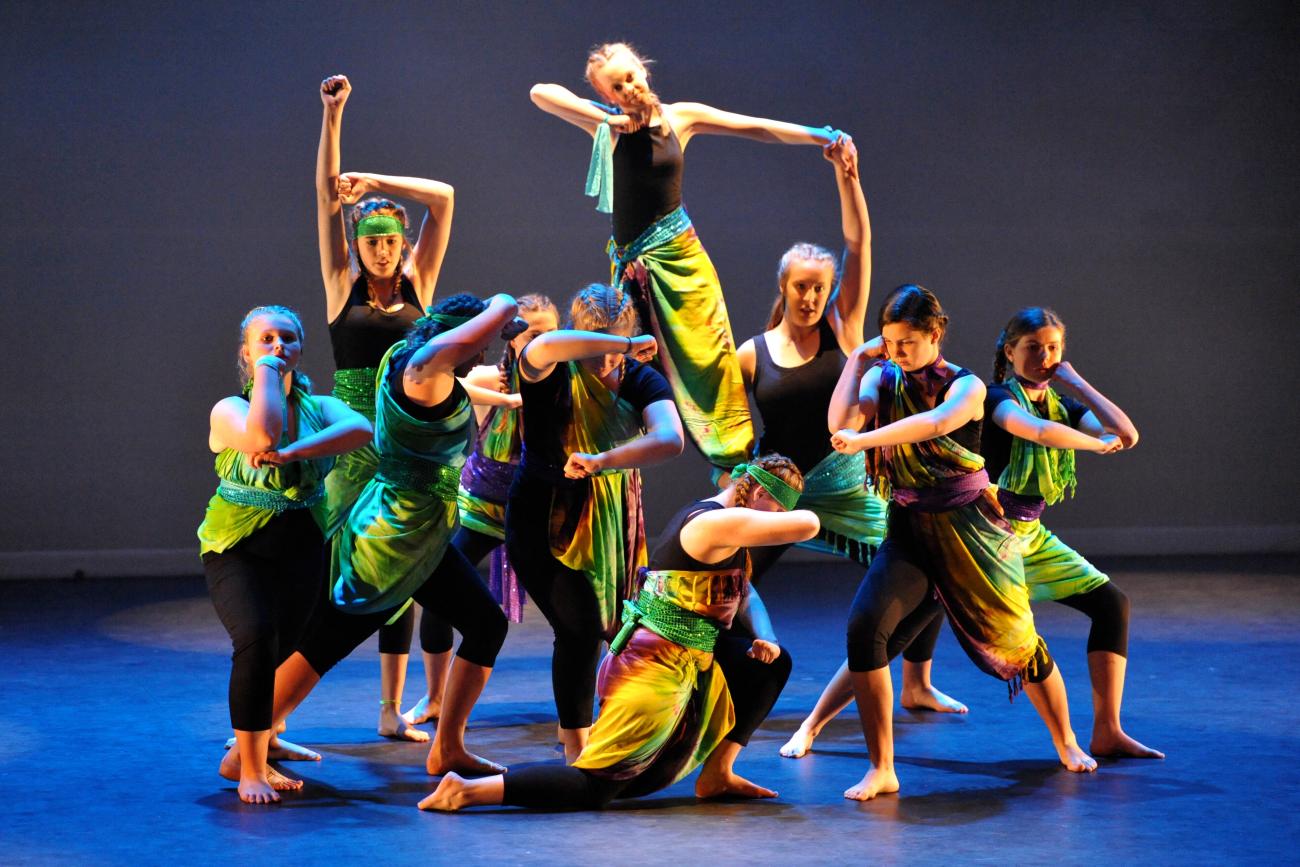 Group of students in a finishing pose wearing black unitards with green material at the festival