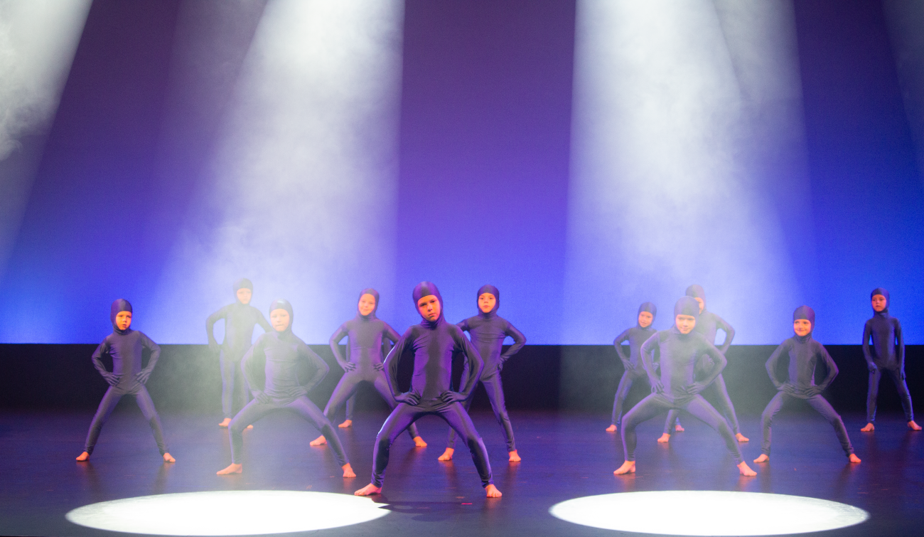 A primary school dance performance with students dressed in purple body suits