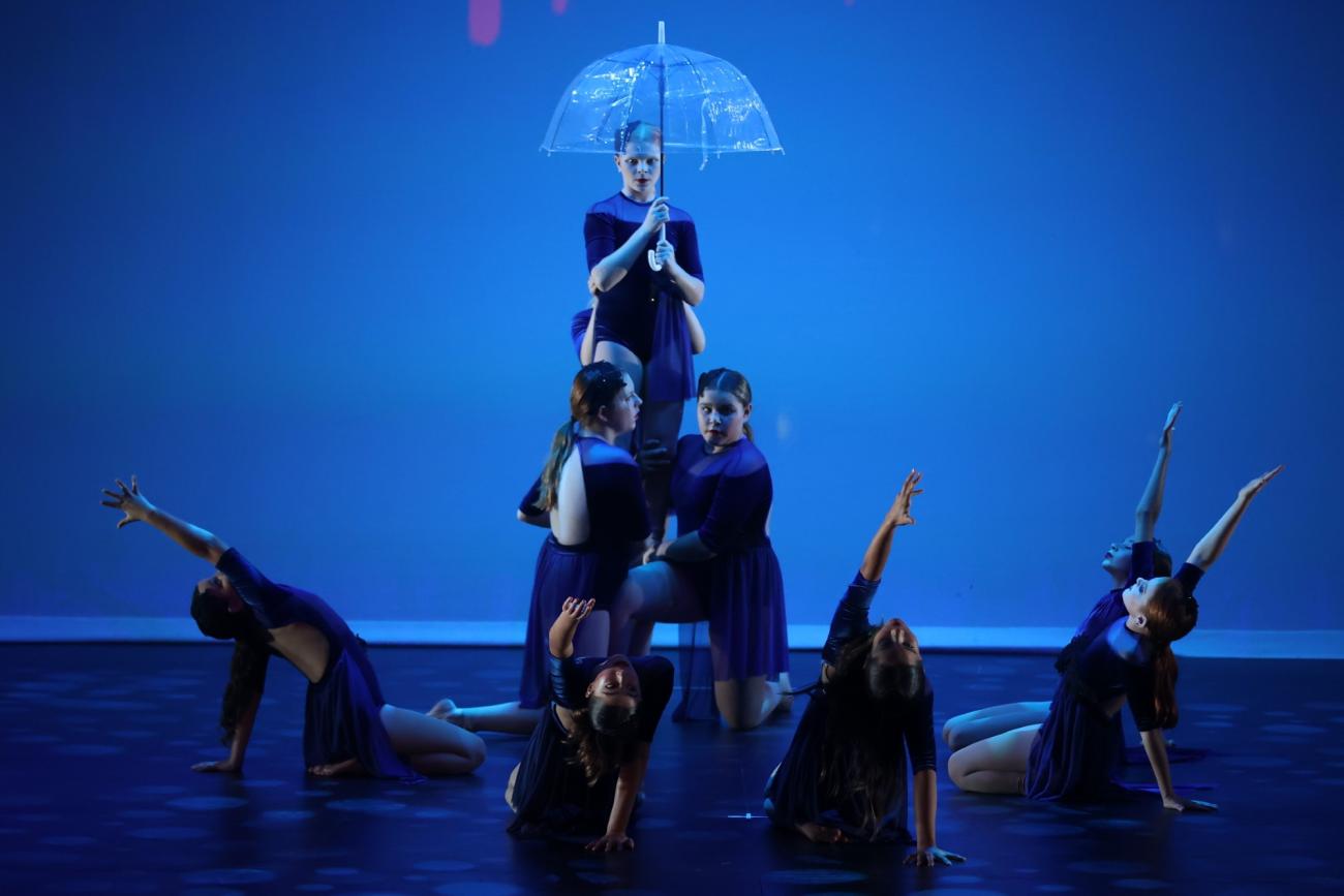 A high school dance performance with student dressed in blue holding an umbrella