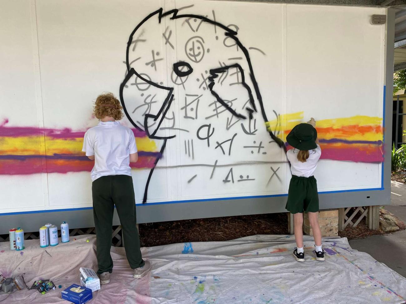Two students painting a mural of a bird