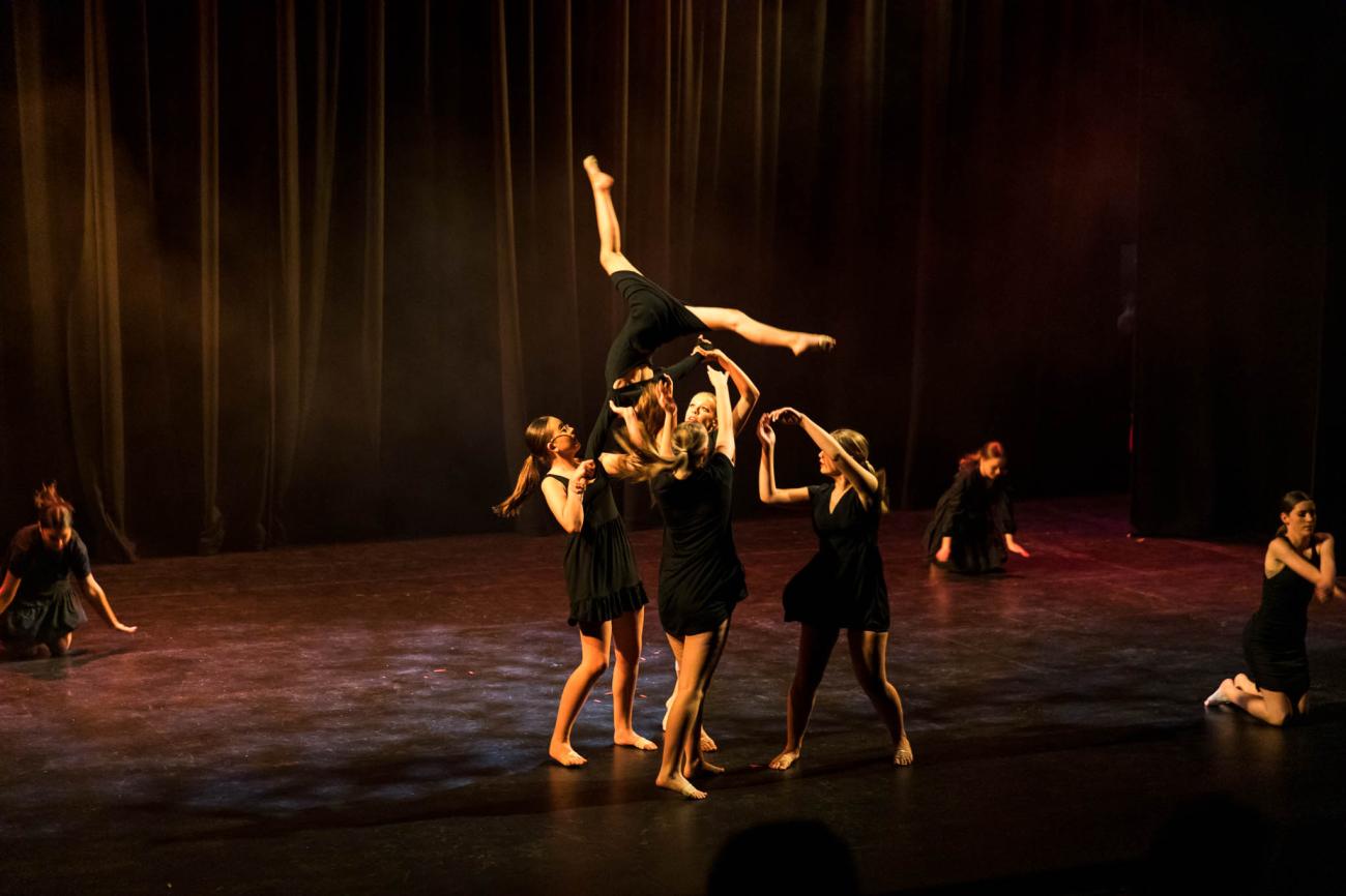 Students in black dresses, 4 students supporting another student to do a lift in air