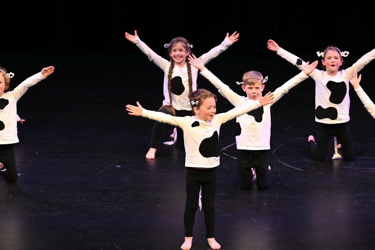 young dancers on stage in cow costumes with arms stretched out