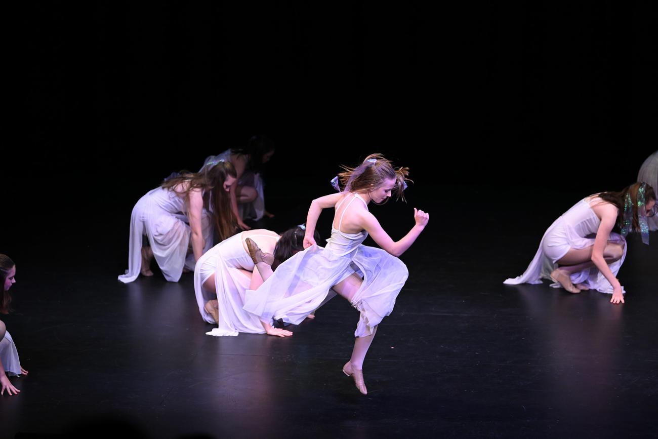 student in white dress doing leap with students behind