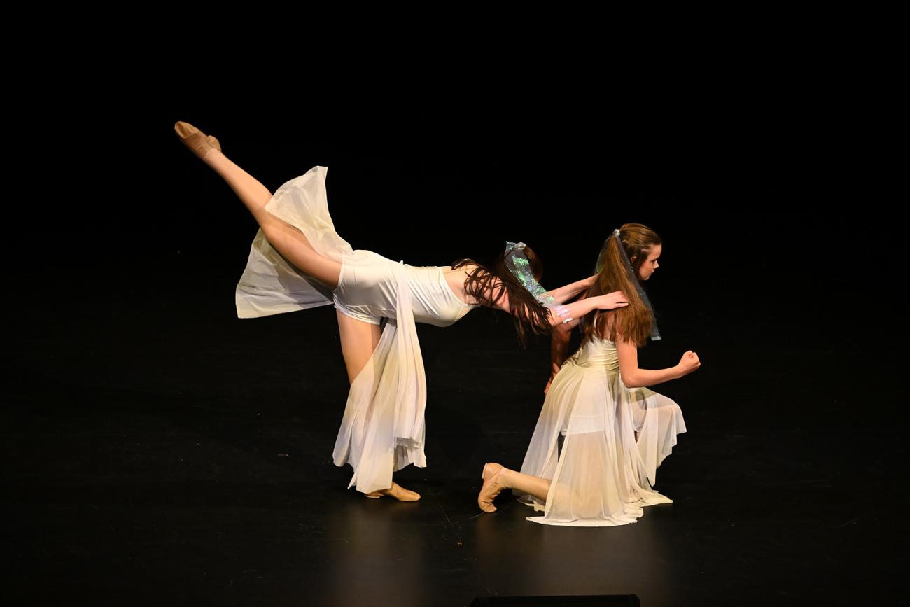 2 students in white dresses in pose on stage