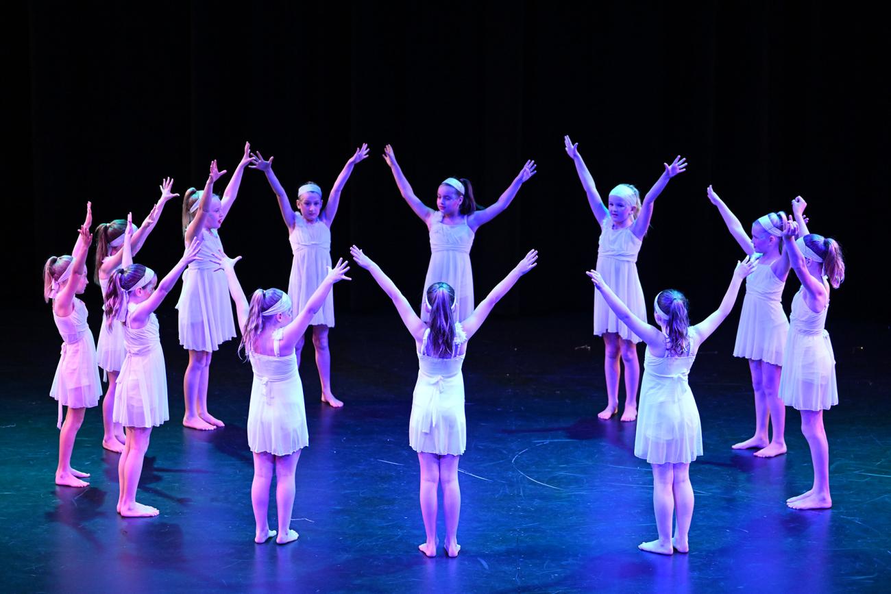 student on stage in a circle in white dresses with arms up