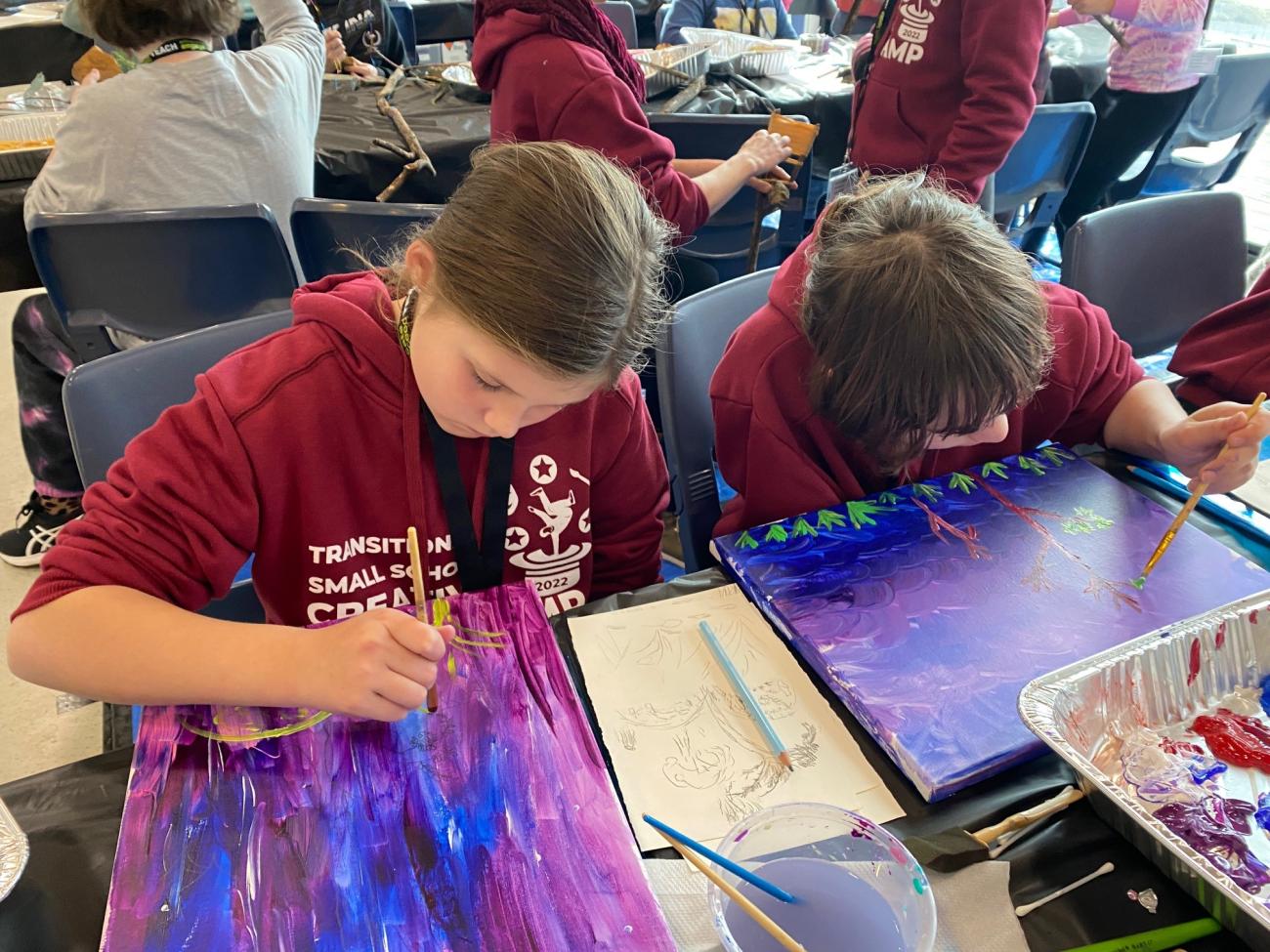 2 students painting on canvases in shades of purple and blue