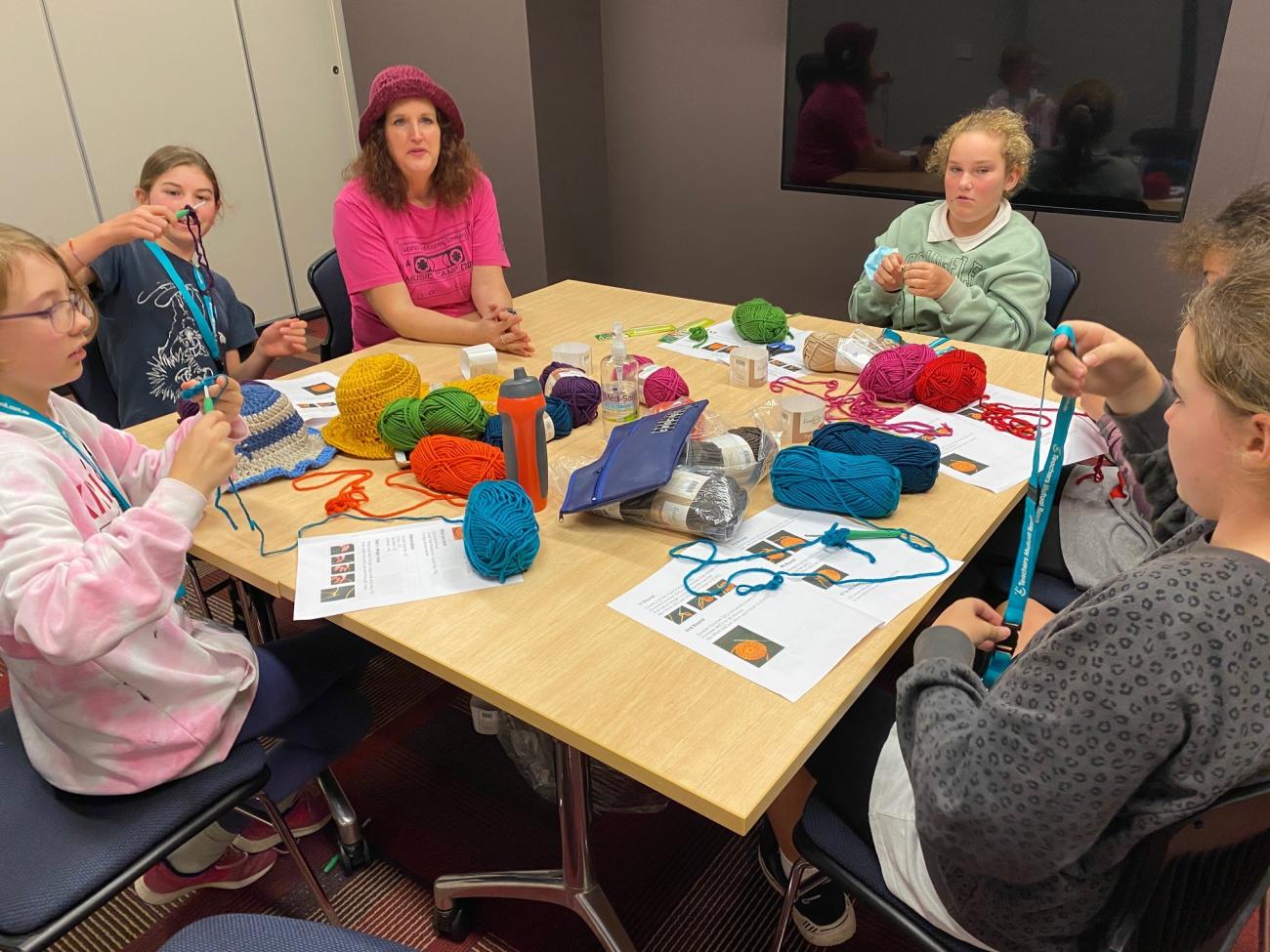 group of students sitting at table with teacher learning to crochet