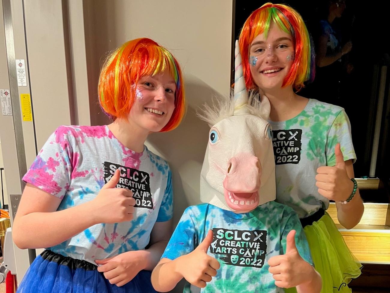 3 students - 2 with orange wigs on and one with a unicorn full face mask