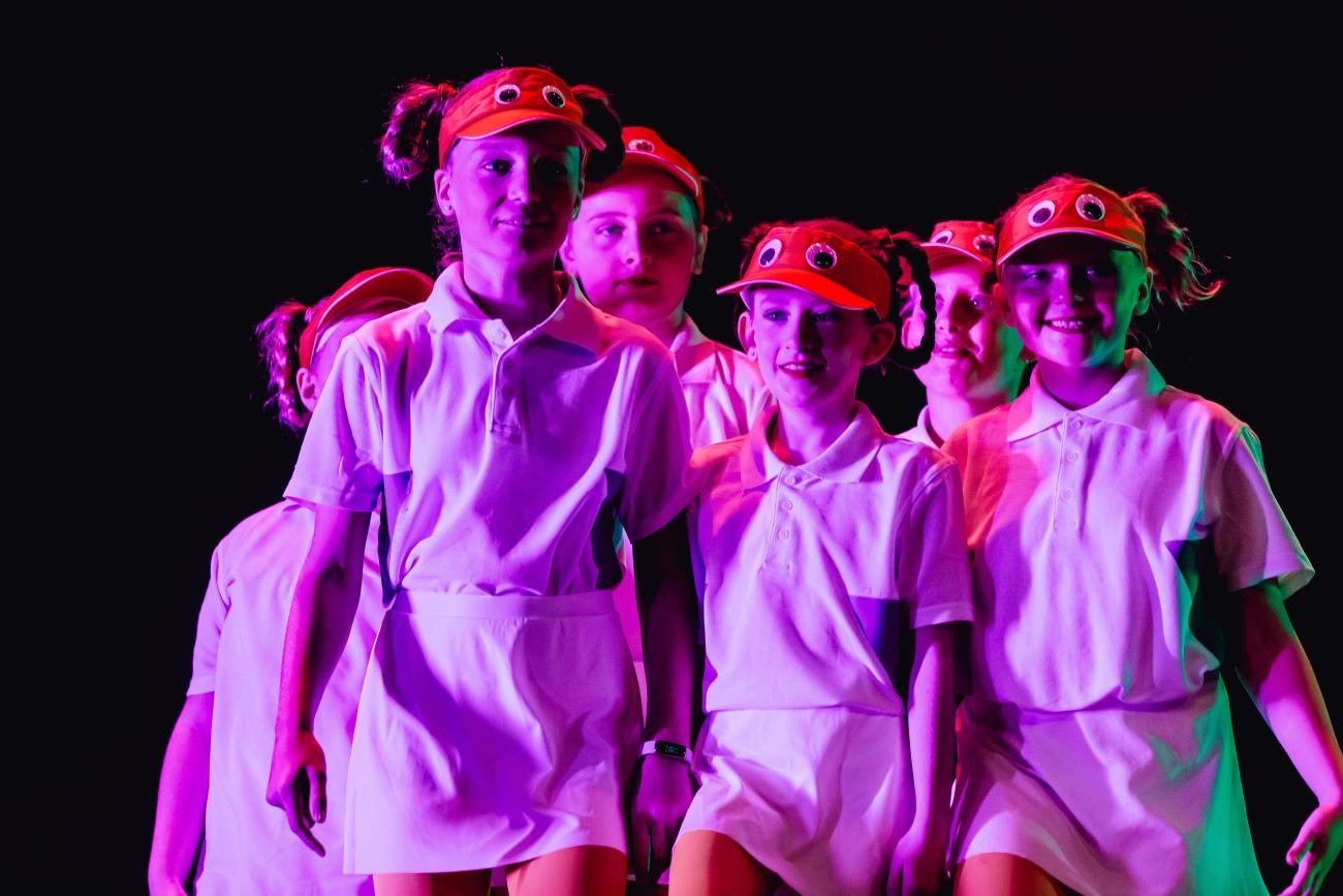 students on stage in white shorts and tshirt and a red hat