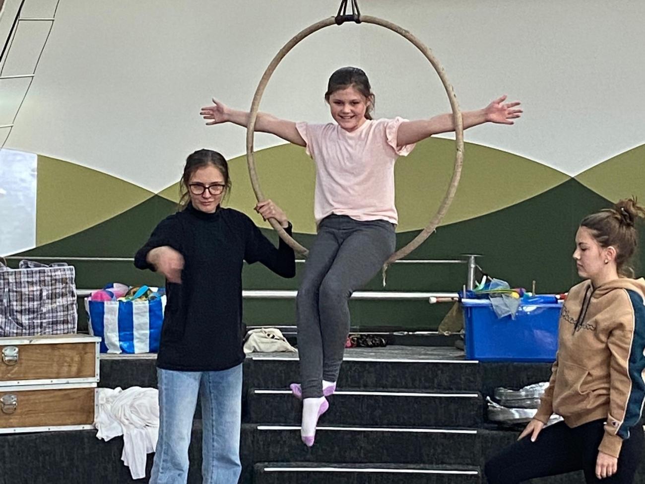young student on circus lyra hoop being supported by 2 older students