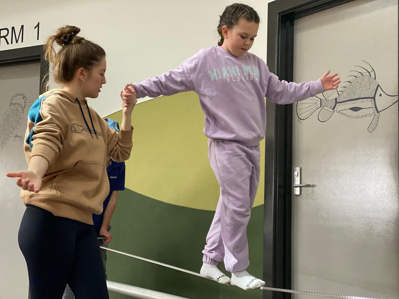 young student walking on tightrope assisted by older student