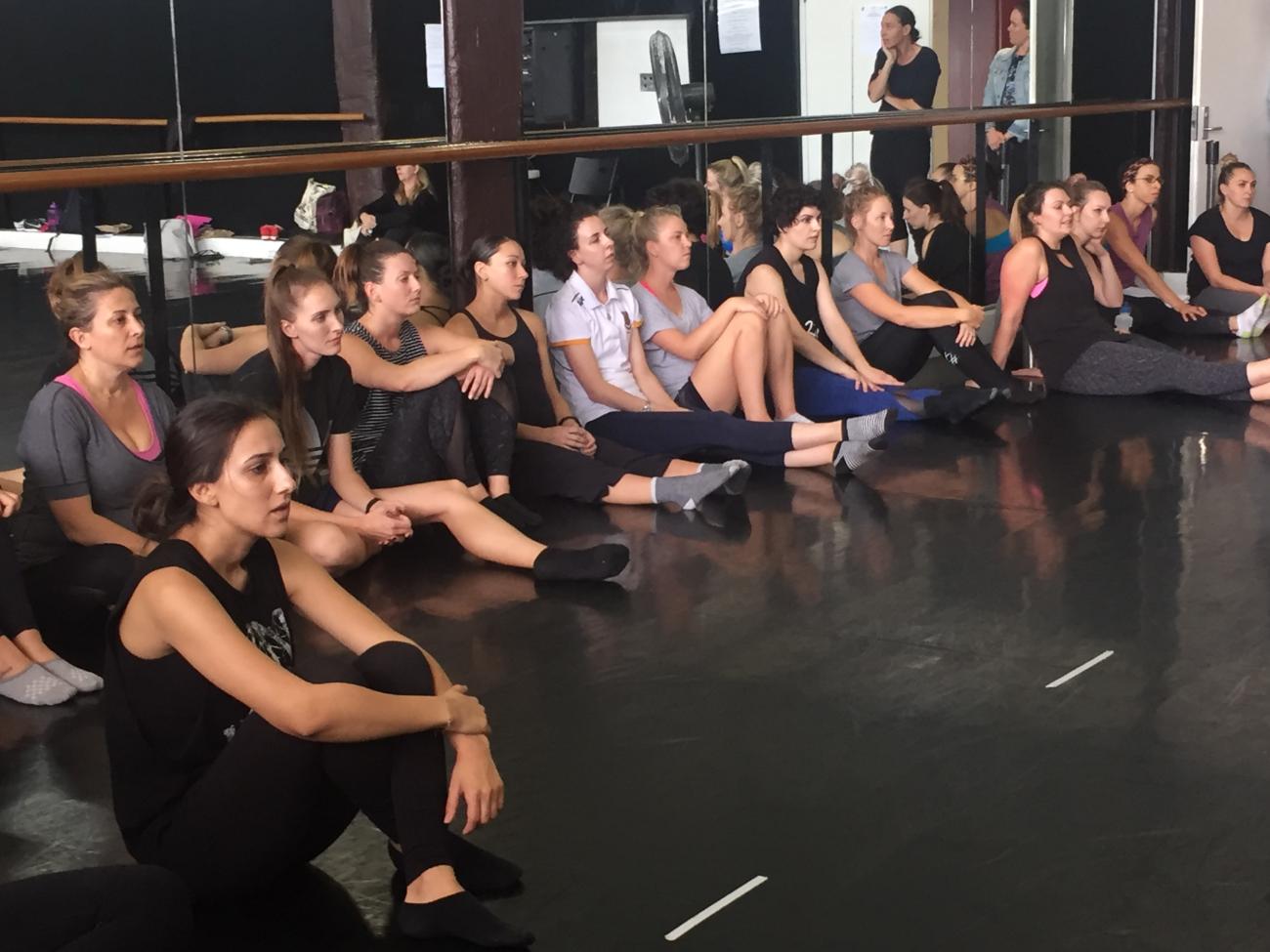 Teachers sitting on the floor in front of mirrors in a dance studio