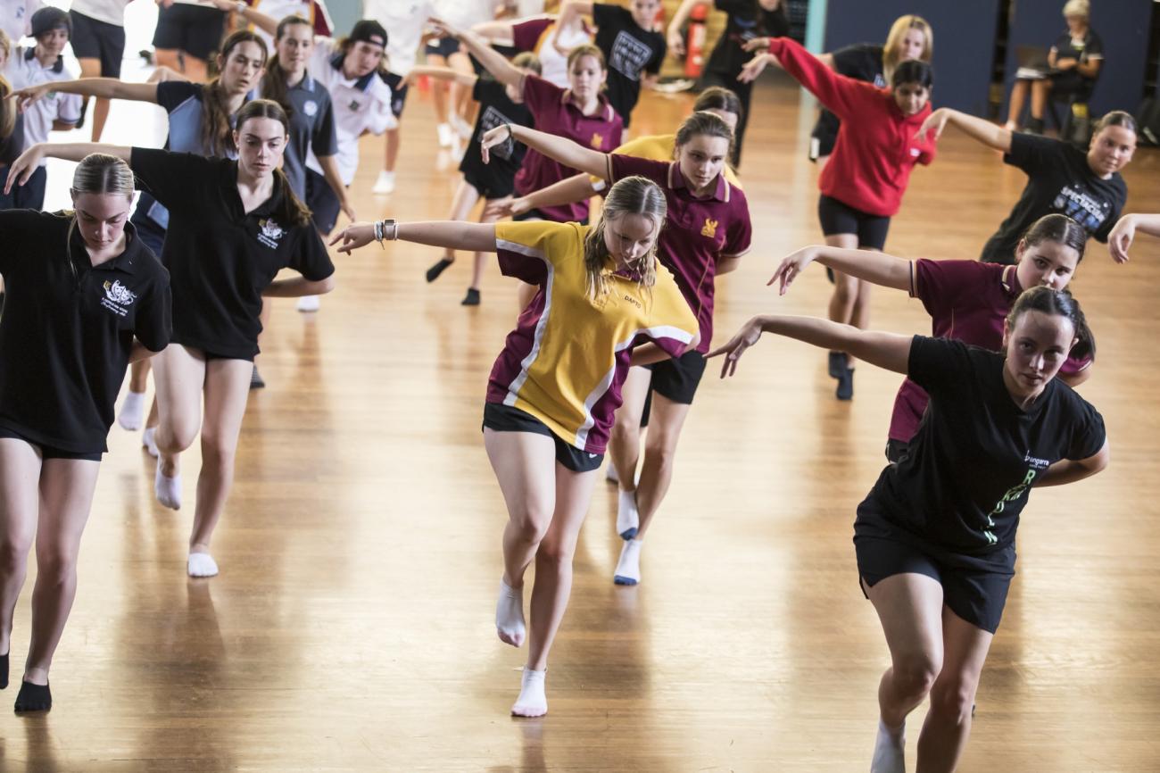 Students dancing with their left arms out-stretched in a school hall