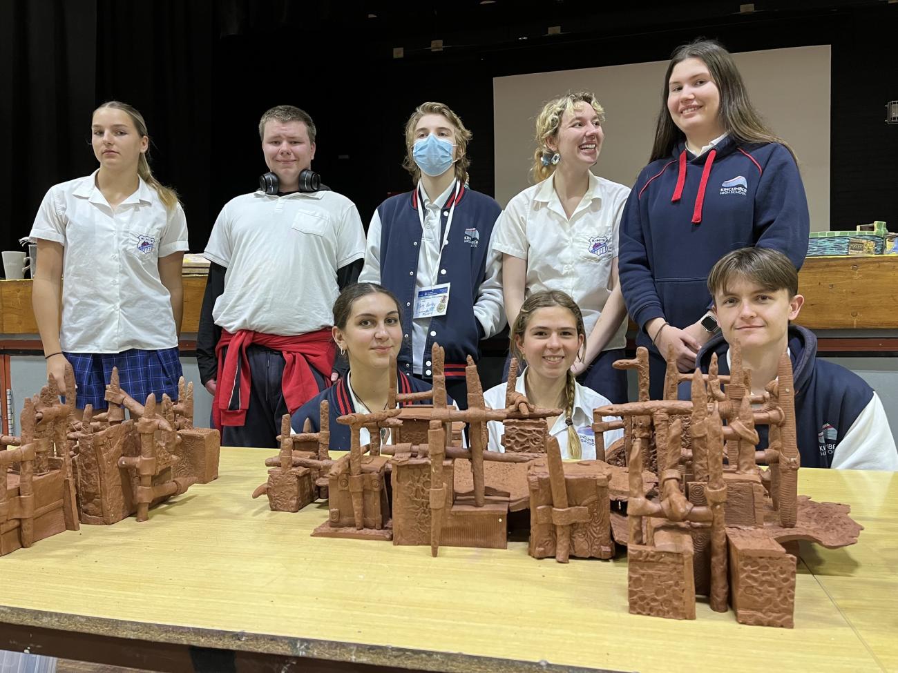 Eight students photographed standing with collaborative clay sculpture