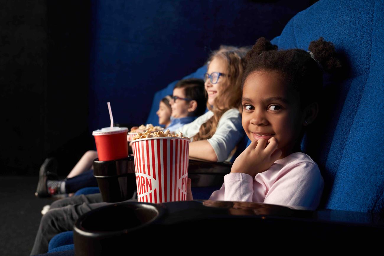 Smiling girl looking at camera holding popcorn at cinema