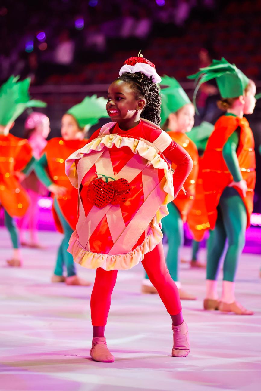 A young smiling dancer wearing a red sequined hat and a sequined apple pie suit costume