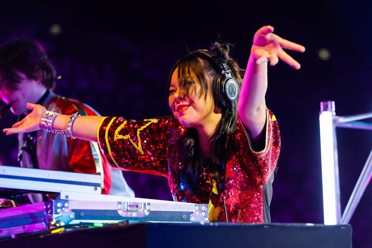A DJ with her arms out, wearing a red sequined shirt and black headphones