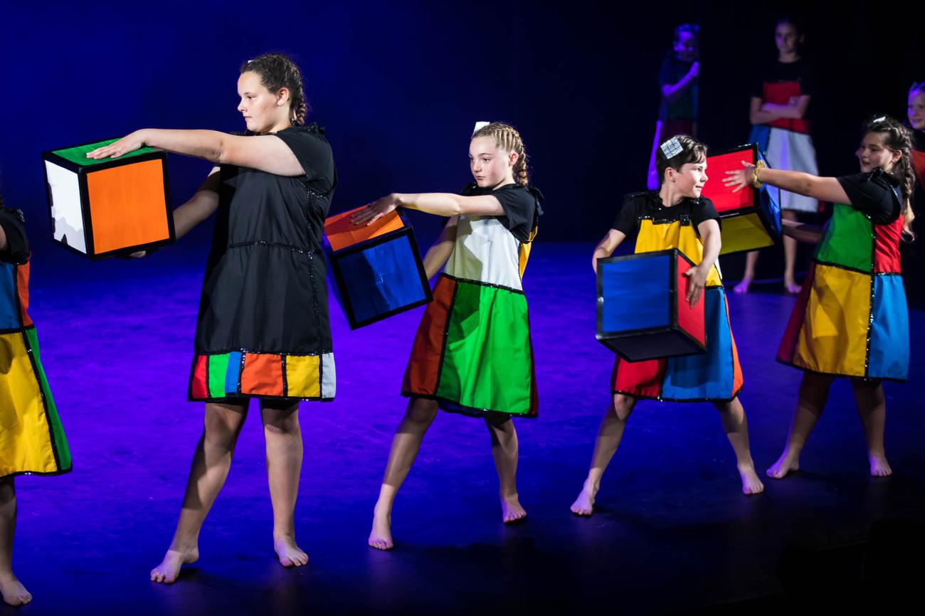 4 dancers onstage in line holding rubic cube pieces.