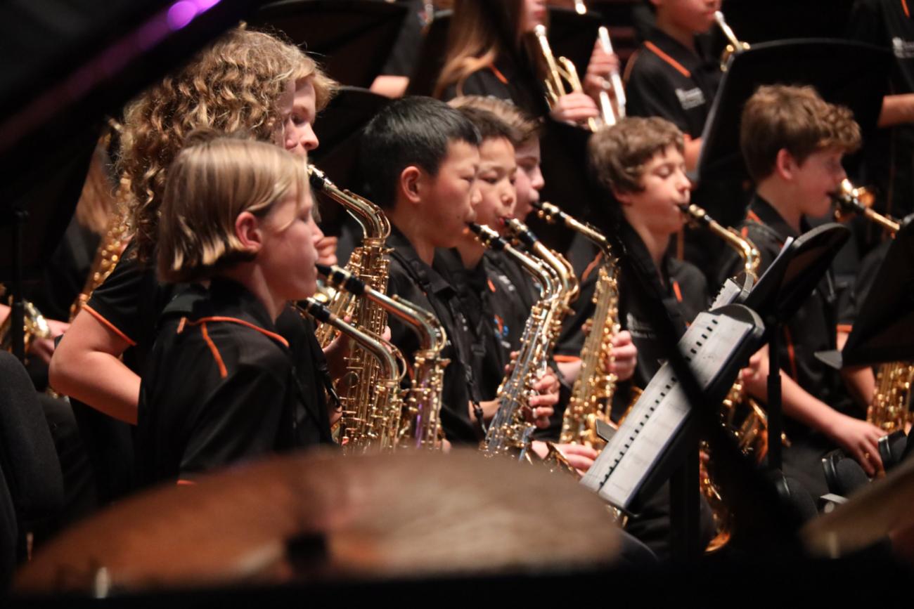 Students seen in profile, playing saxophones on stage.