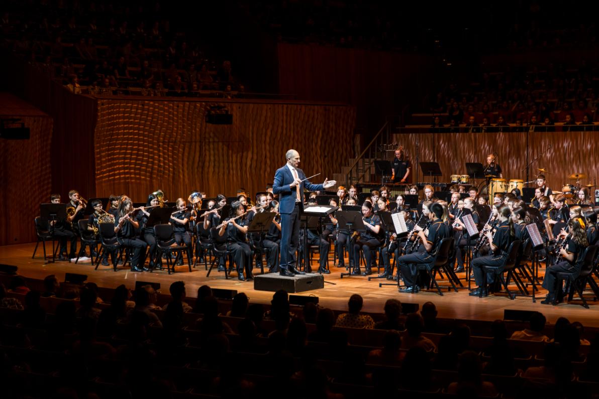 A conductor on stage directing a student orchestra.