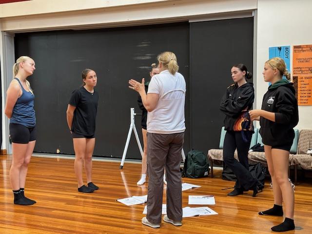 5 students standing around teacher engaging in dance workshop