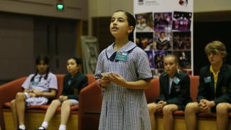 A student at a debating competition, speaking and holding her cue cards.