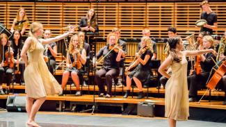 Performance of Firebird Forensics, two dancers in front of an orchestra.