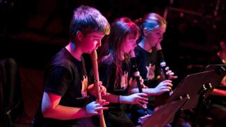 Three students lit with pink light playing recorders