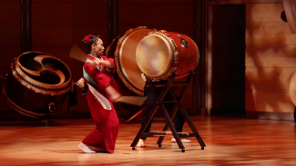Chieko Kojima drumming a large taiko (drum) during a performance of The Beauty Of 8