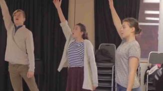 Three drama students in a workshop, holding their right arms up