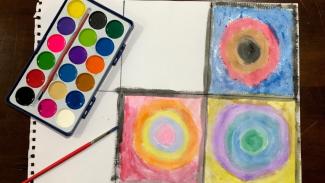 Watercolour paints, a paintbrush, and three painted circles in squares.