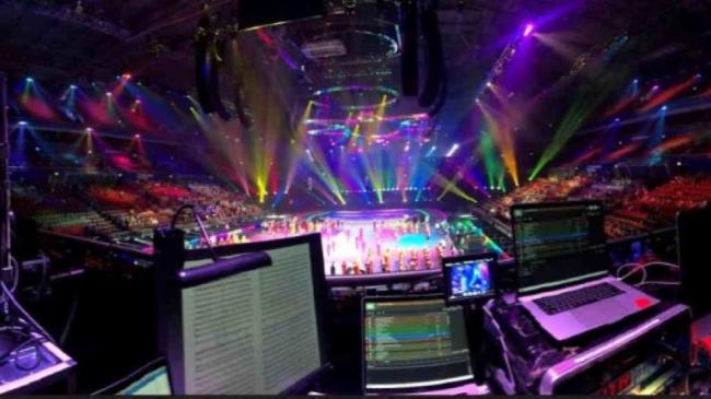 View of a technical rehearsal of Schools Spectacular from sound desk, showing laptops and other audio equipment.