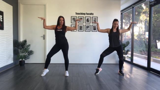 Two dance teachers with their arms out and bent at 90 degrees, and their right leg out with heel off the ground.