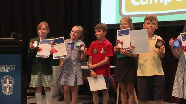Years 3 and 4 students in a line, holding up their certificates and medallions for participating in the NSW Multicultural Perspectives Public Speaking Competition final