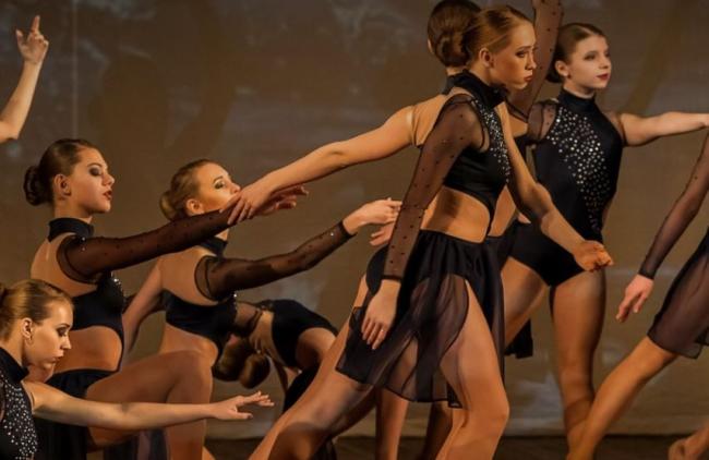 Dancers on stage in black sequin costume in pose of varying heights