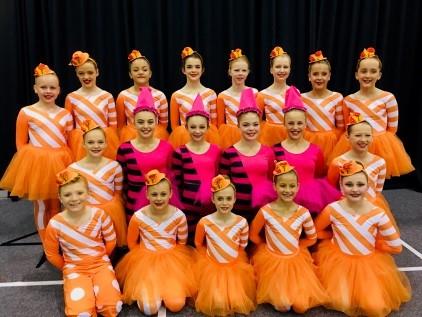 Ensemble students posing for a group photo in orange costumes with white stripes.