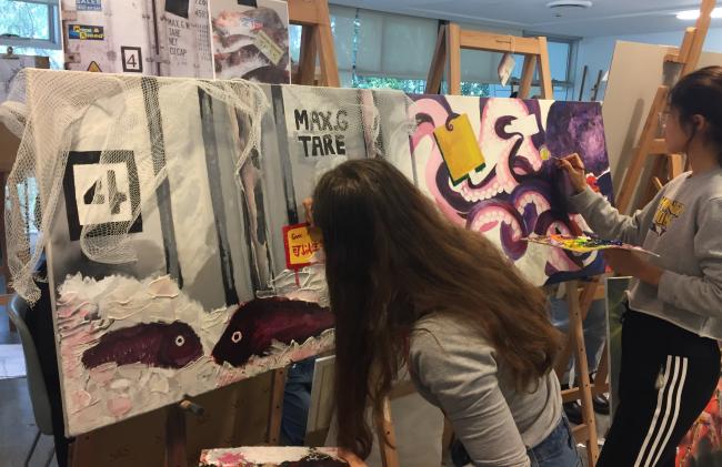 2 female students working on their canvas paintings on an easel