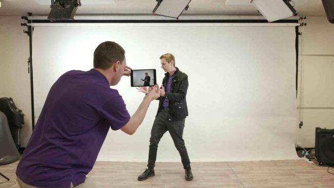 Damien McCabe holding an iPad filming David Todd in front of a white screen